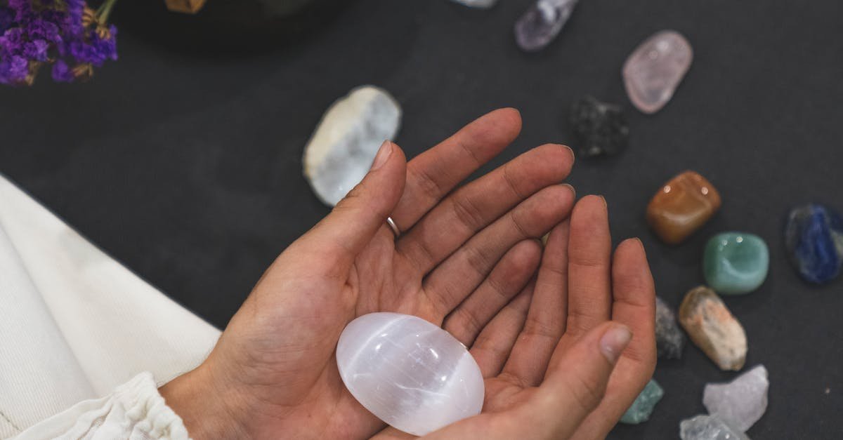 Close-up of hands holding healing stone with tarot cards on surface, promoting spiritual healing.