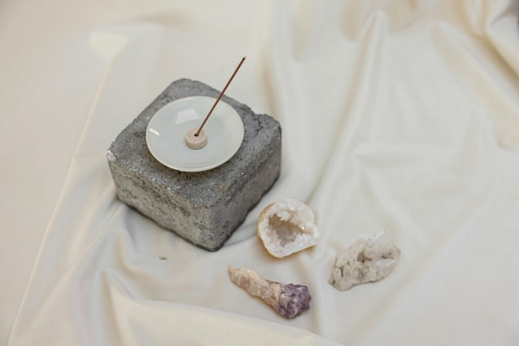 A minimalist setup with an incense stick in a holder and crystals on white linen, offering a sense of inner peace.