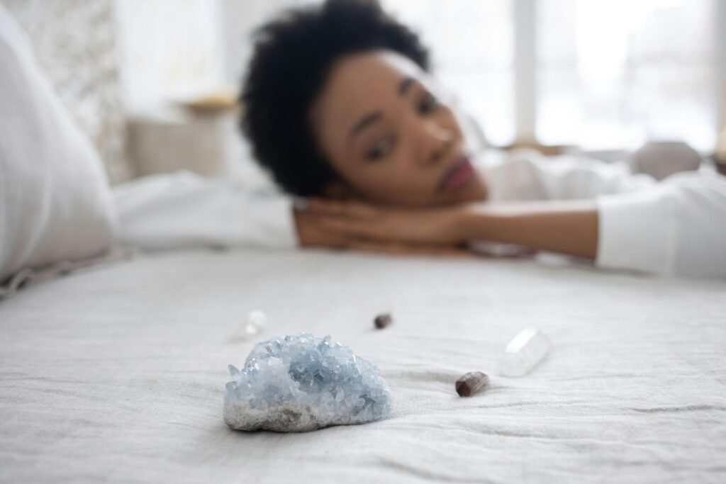 A woman relaxes in a serene bedroom with healing crystals on the bed, capturing a sense of tranquility.