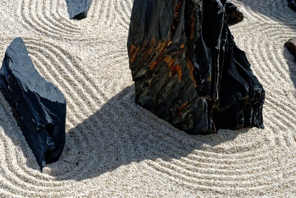 Peaceful Zen garden scene featuring raked sand patterns around dark stones, evoking tranquility.