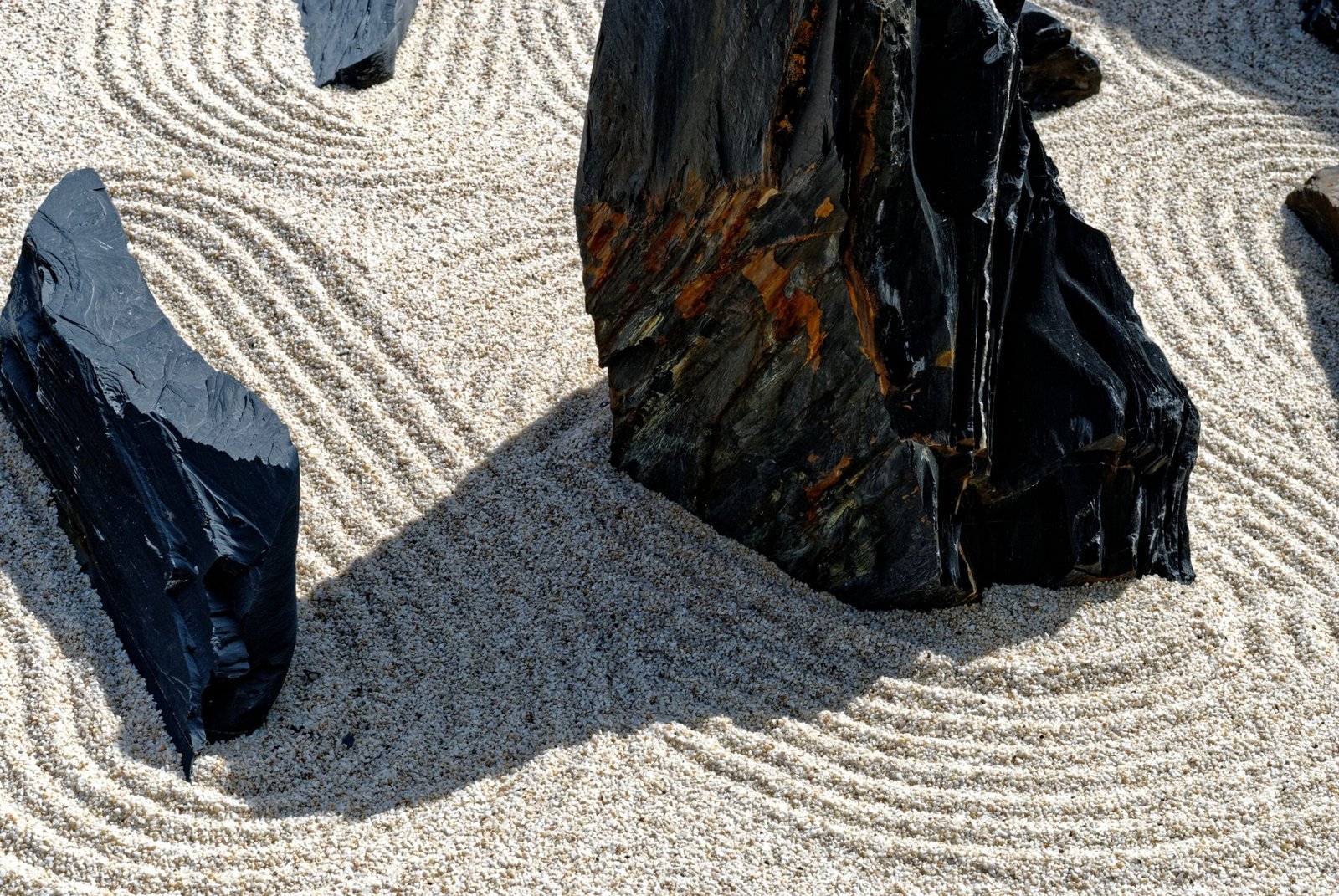 Peaceful Zen garden scene featuring raked sand patterns around dark stones, evoking tranquility.
